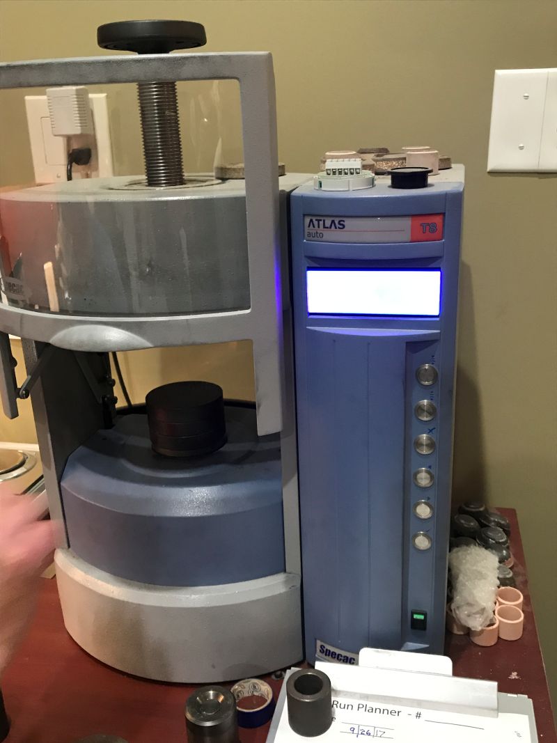 粉末状の炭素に数トンの圧力をかけ、高密度な円柱状に成形する青い自動油圧プレス機