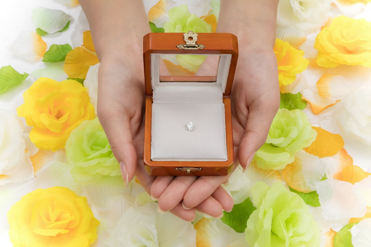 色とりどりのバラに囲まれ、両手で大切に包み込まれた木製ルースケースの中のダイヤモンド